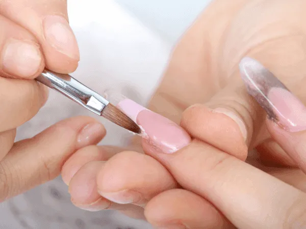 Applicazione di gel costruttore rosa su unghia naturale con pennello professionale a lingua di gatto.