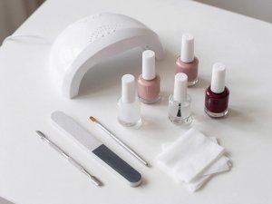 Lampada LED, flaconi di gel, lima, spingicuticole, pennello e salviette su un tavolo bianco